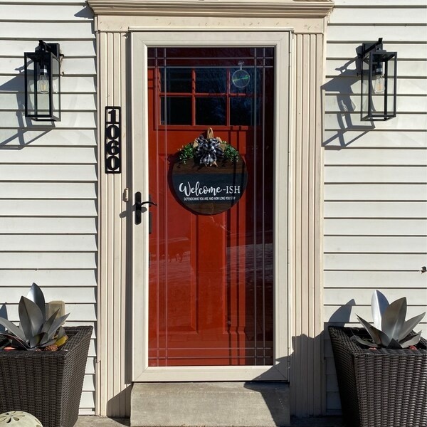 Two low steel flower sculptures in dark planters flanking a red front door