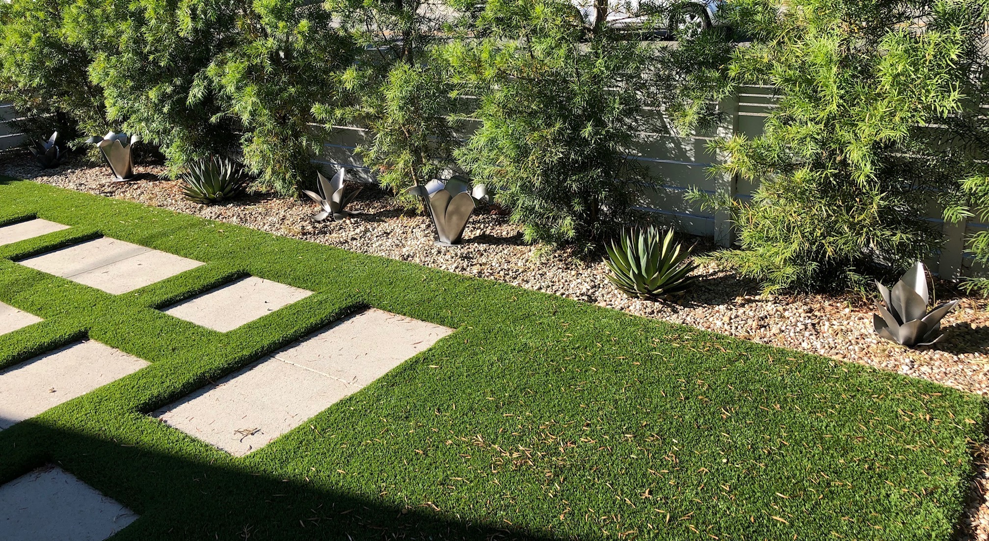 Wide view of steel flower sculptures spaced along the edge of a lawn