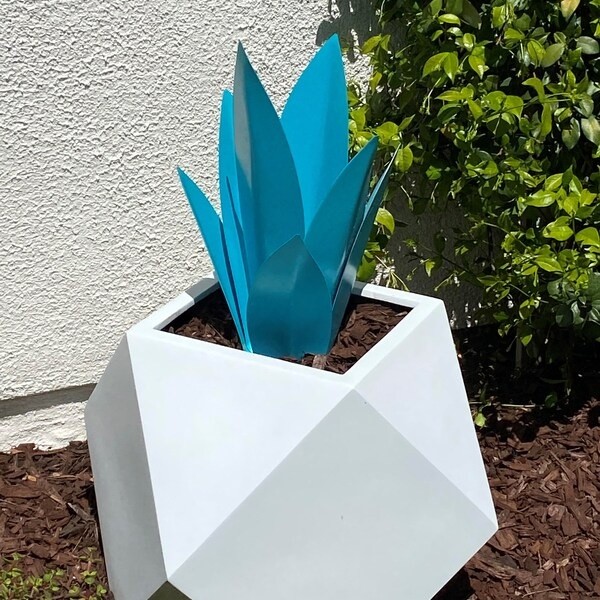 Turquoise steel sculpture in a white geometric planter against a pale wall