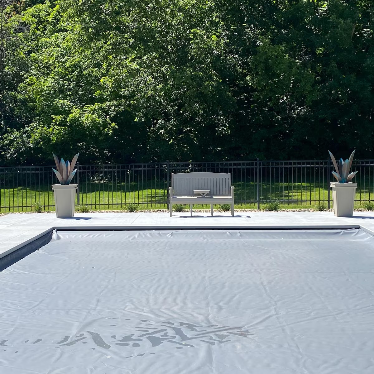 Two steel agaves in tall planters on opposite sides of a bench beside a covered pool