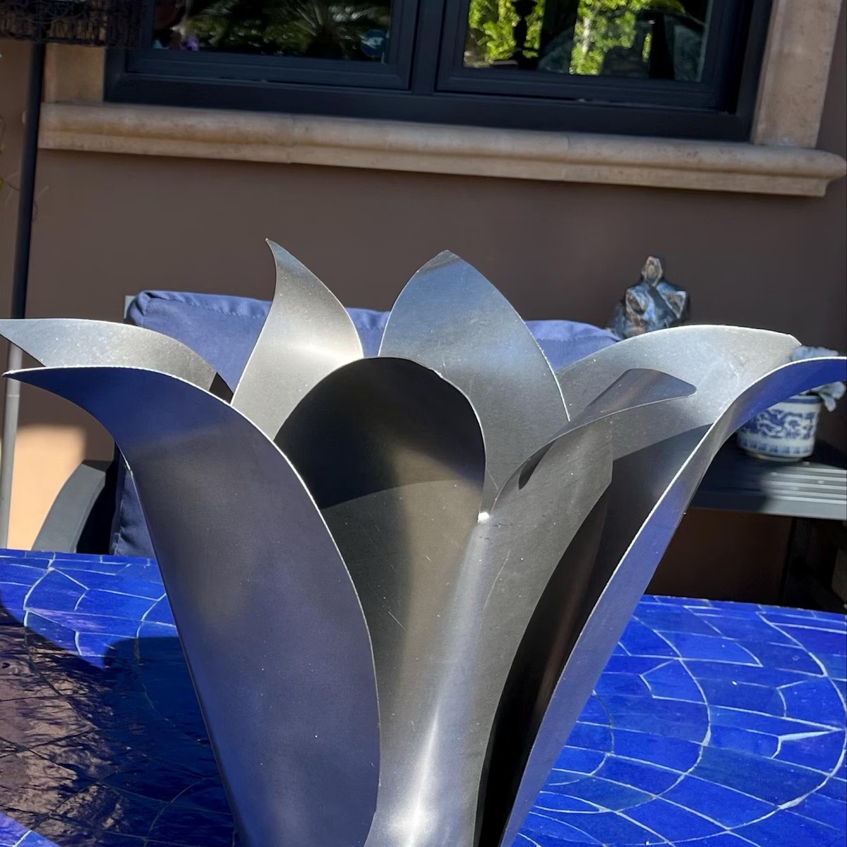 Silver steel Blossom on a blue-covered table beneath a window